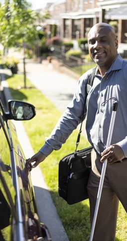 Picture of a blind person approaching his car with the help of a walking stick. 
