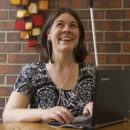 Picture of a blind person using a laptop and listening to audio using a headset. 